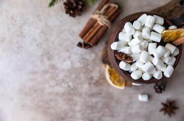 Brown ceramic mug with hot chocolate or cocoa with marshmallows, cinnamon stick, anise and dry orange slices on wooden board. The concept of fall or winter time. Top view.