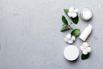 Organic cosmetic products with cotton flower and green leaves on cement background. Copy space, flat lay