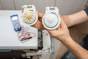 A new and old pumps for dishwasher in the hands of a men, against the background of a disassembled...