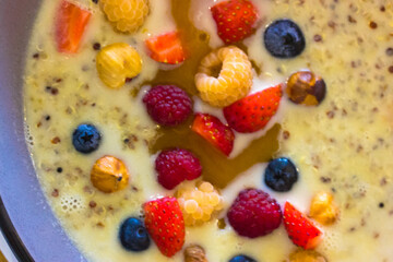 Porridge quinoa with coconut milk, honey and fresh fruit, berries top view. Strawberries, blueberries, yellow raspberries, nuts flat lay. Healthy food concept. Delicious organic breakfast. Trendy meal