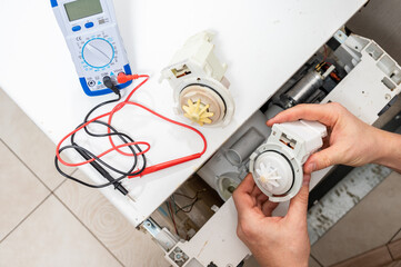 A new pump for dishwasher in the hands of a men, against the background of a disassembled dishwasher