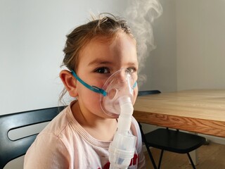Sick adorable preschool girl with nebuliser mask at home. Treatment for bronchitis with inhaling...