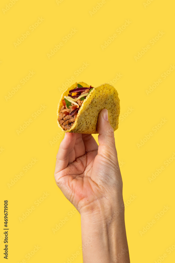 Wall mural Hand holding a Mexican taco beef on yellow background