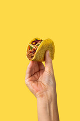 Hand holding a Mexican taco beef on yellow background - obrazy, fototapety, plakaty