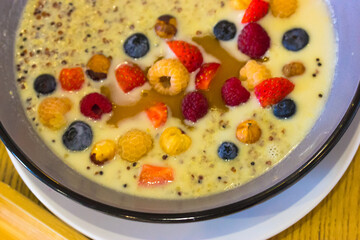 Porridge quinoa with coconut milk, honey and fresh fruit, berries top view. Strawberries, blueberries, yellow raspberries, nuts flat lay. Healthy food concept. Delicious organic breakfast. Trendy meal