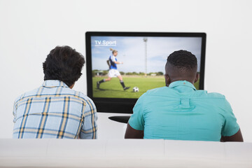Rear view of two friends sitting at home together watching football match on tv