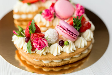 The cake with cheese cream and honey cakes is decorated with flowers, berries and sweets. A cake in the shape of the number 3