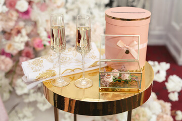 A box with wedding rings and gold sequins, champagne glasses, flowers.