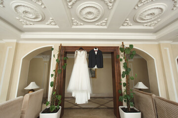 Fototapeta na wymiar The bride's wedding dress and the groom's jacket on wooden hangers, hang on the wardrobe.