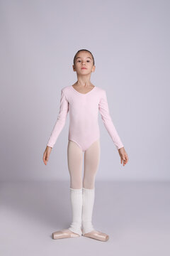 Little ballerina practicing dance moves on grey background