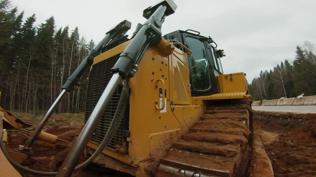 Crawler bulldozer levels ground, preparation surface for construction of new road, hydraulic blade of heavy grader rakes soil, in front onboard POV shot. Earthmover on work