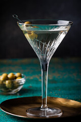 Dirty martini cocktail in martini glass with olives garnish on green colored table