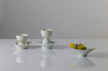 Still life of Chinese antique white porcelain cups and bowl with branch of white grapes on white table