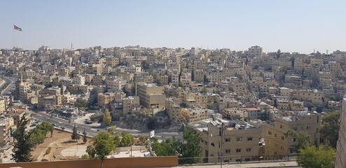 Fototapeta na wymiar Vue générale et en hauteur de la ville d'Amman, la capitale de la Jordanie, zone chaude, urbaine et torride, petites maisons cubiques et anciennes, avec drapeau et un peu de végétations secs 