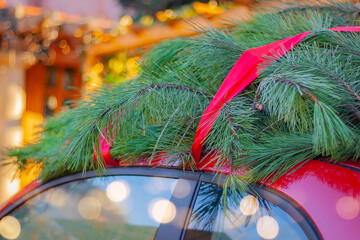 close-up christmas tree tied with a red ribbon on the roof of a car in the street