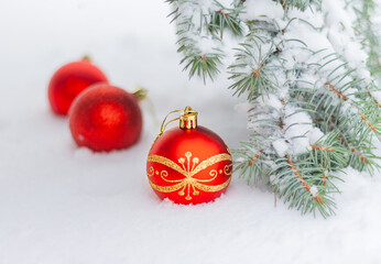 red christmas baubles lie in natural snow near fir branches