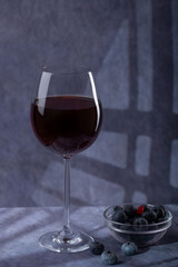 A simple still life. A beautiful glass with red wine and a plate with blue berries on a dark background with creative lighting