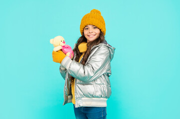 smiling teen girl hold toy bear. child wearing warm clothes on blue background.