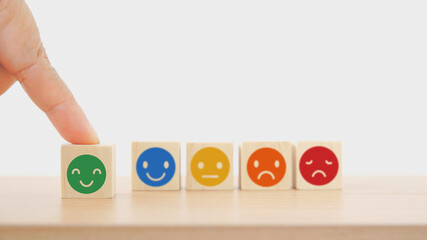 hand choose green smiling face on wooden block with other blurred face, customer review, feedback, rating, ranking for service or product, mental health concept