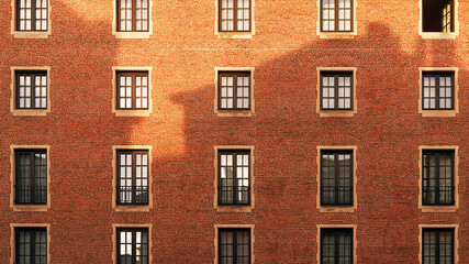 Fototapeta na wymiar Old red brick wall with windows and shadow of another building at sunset
