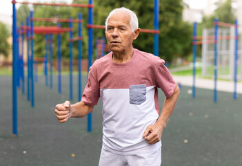 Senior man running on jogging track in nature. Healthy retirement lifestyle