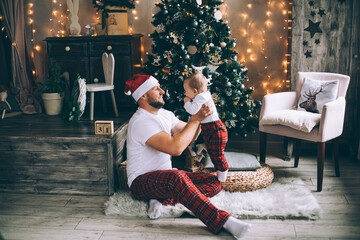 Obraz premium Smiling man holding his baby while playing near Christmas tree