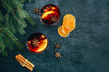 top view of a drink mulled wine with orange and star anise eoritsa sticks in a transparent glass on a dark concrete background decorated with branches of a Christmas tree with free space for text