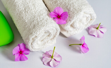Clean white rolled towels with flowers and green soap on white