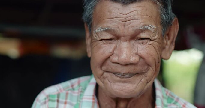 An Asian man who is more than seventy years old and works as a wage earner in a farm, live in a poor house, smiling and laughing happily.