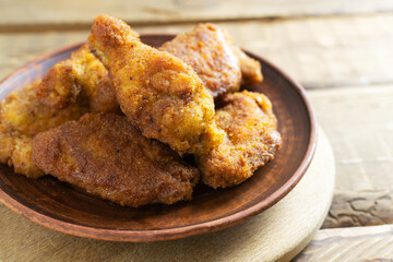 Crispy chicken wings and legs, breaded, cooked in oil in a ceramic plate on a wooden background. Junk food concept.