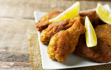 Crispy breaded chicken wings and legs with lemon slices on a wooden background. Junk food concept. Horizontal orientation. Selective focus. Copy space.