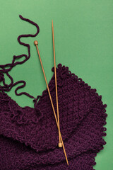 Vertical image of purple knitted scarf.wooden pins on the green background.Type of home hobby
