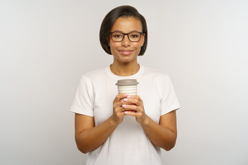 Studio portrait of african american female holding paper coffee cup. Young woman in white t-shirt with hot beverage in portable takeaway mug. Coffee-to-go drink and eco-friendly reusable glass concept