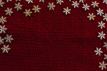 Fototapeta na wymiar Golden snowflakes on red knitted background. Winter holidays concept. Snow winter fantasy. Christmas décor. Christmas greeting card or New Year card. Top view. Flat lay. Place for text. Copy space.