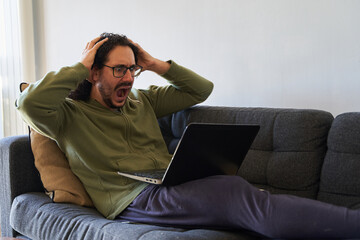 Stock market crash concept of young man screaming at laptop on the sofa