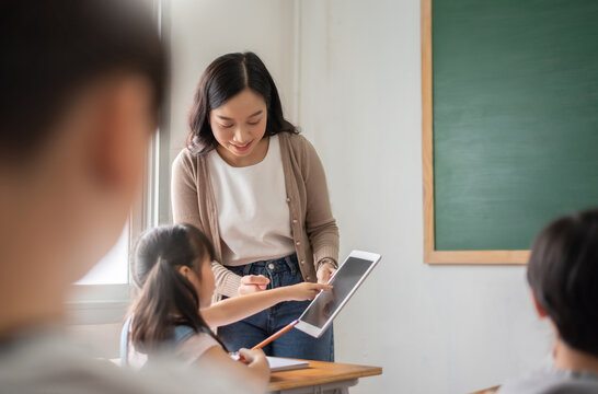 Asian Beautiful female teacher teaching Asian girl learning with digital tablet in classroom