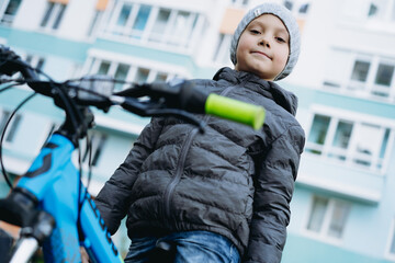 close up portrait of cute caucasian boy on bicycle. apartment building on background