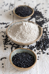 Bowls with black lentils flour and beans on white wooden table close up