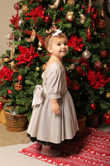 beautiful little girl in a festive dress stands by the christmas tree