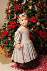 beautiful little girl in a festive dress stands by the christmas tree