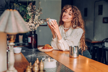 Smiling young woman with curly hair wearing vintage style drinking tea