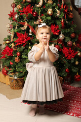 beautiful little girl in a festive dress stands by the christmas tree