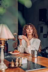 Young woman with curly hair wearing vintage style drinking tea