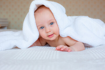 Fototapeta na wymiar baby boy after bathing wrapped in a white towel, lying in the bedroom on the bed at home