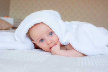 baby boy after bathing wrapped in a white towel, lying in the bedroom on the bed at home