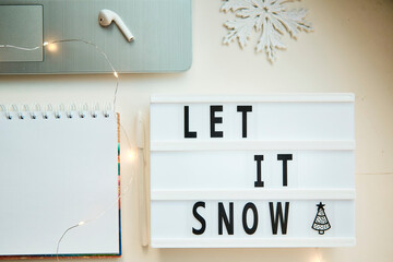 Mockup of notebook with New Year's decorations. Text Let it snow and laptop. The concept of New Year's decisions and resolutions with setting goals for the year. Bokeh on foreground. Christmas mock up