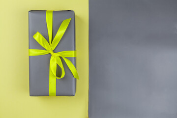 The gift is packaged in perfect gray on a yellow background and a gray background. The trend colors are yellow, gray. Copy space. View from above.