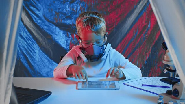A Little sientist in protectiva mask is working with tablet in a laboratory.