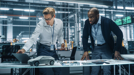 Two Automotive Engineers Working in Office at Car Factory. Industrial Designer Shows Conceptual Electric Engine Parts to Colleague, Discussing Different Applications in Technological Laboratory.