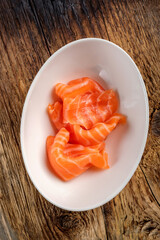 Pieces of fresh salmon sashimi in a white bowl on a wooden background. Salmon fillet for sushi, top view